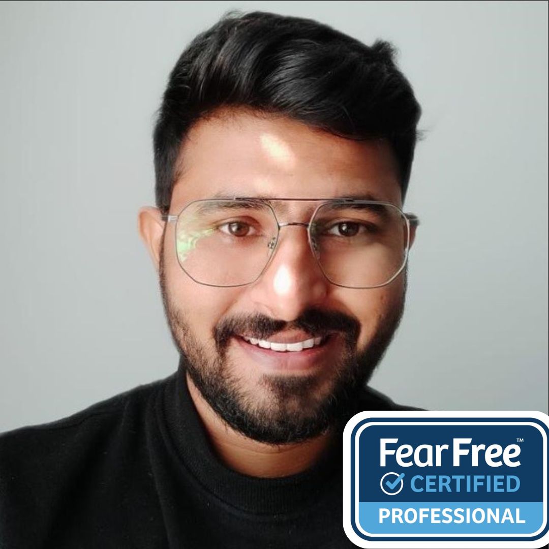 Parth, a Veterinary Assistant at Waterloo West Animal Hospital, smiles warmly in a close-up portrait against a plain light-gray background. He wears glasses and a black sweater, with a “Fear Free Certified Professional” badge displayed in the corner, reflecting his gentle and compassionate approach to animal care.